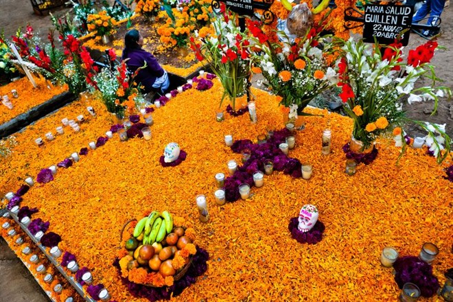 Một phụ nữ Mexico ngồi bên cạnh ngôi mộ được phủ đầy hoa cúc vạn thọ và một số loại hoa tại lễ hội ở Tzintzuntzan, Mexico. (Nguồn: NatGeo)