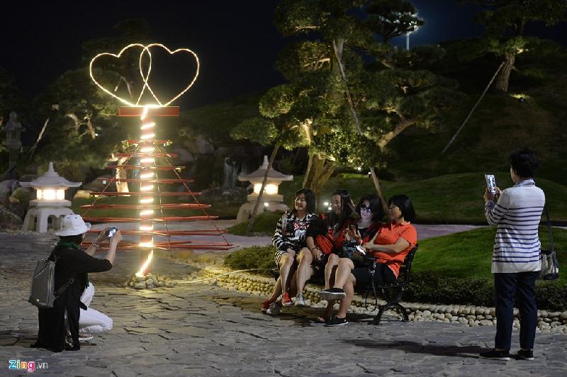 Du khách thích thú chụp ảnh bên mô hình cây thông với đôi trái tim sáng lung linh trong đêm.