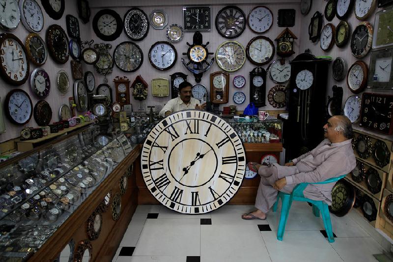 Bán thời gian: Một người đàn ông bán đồng hồ nói chuyện với khách hàng trong cửa tiệm ở Islamabad, Pakistan. Ảnh: Reuters.