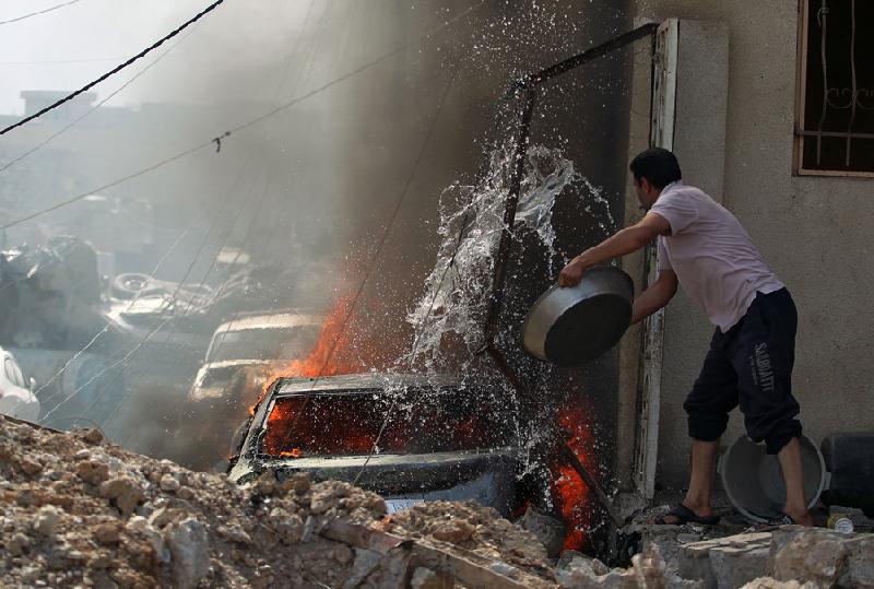 Còn nước còn tát: Người dân Iraq cố gắng dập lửa từ một chiếc ôtô đang bốc cháy dữ dội ở Mosul, trong cuộc chiến chống lại tổ chức Nhà nước Hồi giáo tự xưng (IS). Ảnh: AFP.