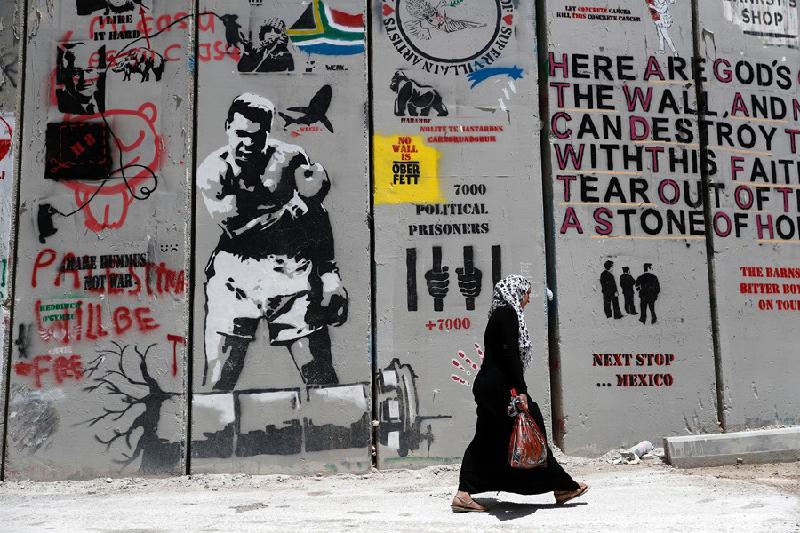 Hai thế giới: Người phụ nữ Palestine đi bộ ngang bức tường ở khu vực Bờ Tây Bethlehem. Cách đó chưa đến 10 km, bên kia bức tường, ở thành phố Jerusalem, Tổng thống Mỹ Donald Trump sẽ có chuyến công du đầu tiên tới Israel vào ngày 22/5. Ảnh: AFP.