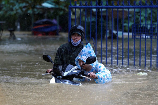 Người dân vật lộn dắt xe trong bão lũ khi nước ngập gần đến cổ (Ảnh Reuters)